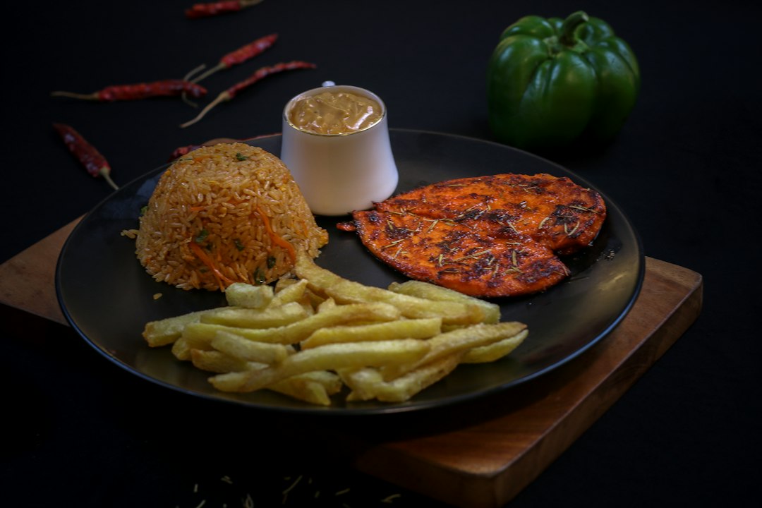 Grilled chicken, rice, fries, and sauce on a dark plate