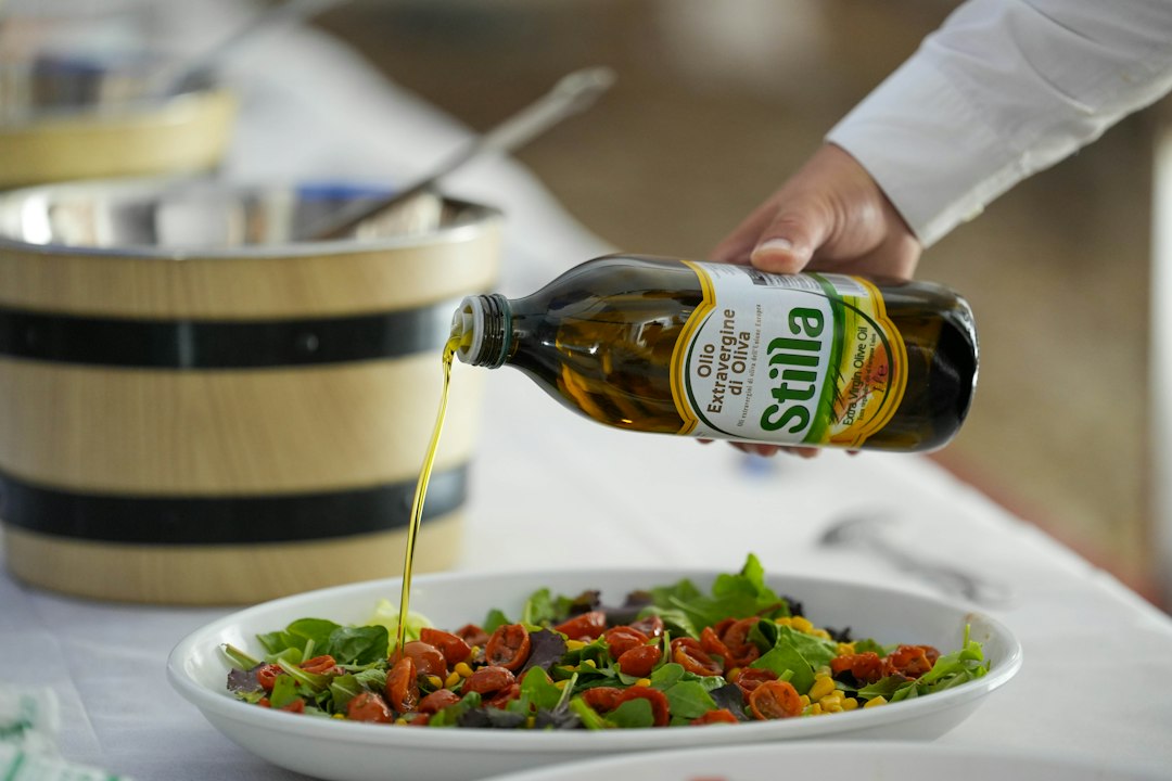 Hand pouring olive oil onto a fresh salad